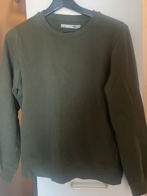 Olivgrön sweatshirt med rund hals - En basic olivgrön sweatshirt med rund halsringning och långa ärmar. Tröjan har ribbade muddar vid ärmslut och nederkant. Perfekt för en avslappnad och stilren look.