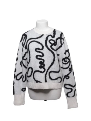Vit stickad tröja med svart mönster - Säljer en vit stickad tröja med unikt svart abstrakt mönster. Tröjan har rund hals, långa ärmar och ribbade muddar vid ärmslut och nederkant. Perfekt för dig som gillar statement-plagg och vill sticka ut lite extra.