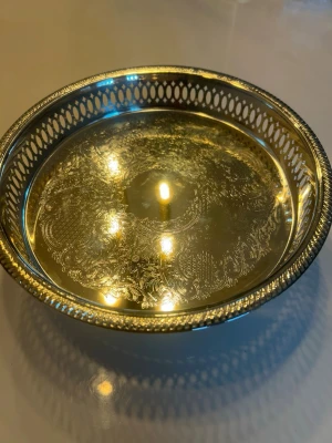 Dekorativ skål i mässing - Snygg rund skål i mässing med vackert graverat mönster och genombruten kant. Perfekt som dekoration eller förvaring av småsaker. Skålen har en klassisk design och glänsande guldfärg. 