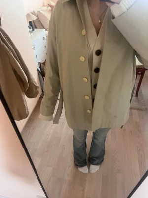 Beige kappa från Filippa K - Stilren beige rock med stora ljusa knappar och rak passform. Rocken har krage och är tillverkad i ett slätt tyg som ger en clean look. Perfekt för dig som gillar minimalistisk stil och vill ha en enkel men snygg jacka till vardags.