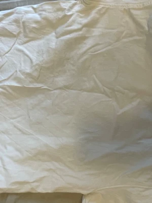 Vit Real Madrid Mbappé tröja - Säljer en vit fotbollströja från Real Madrid med Mbappé och nummer 9 tryckt på ryggen. Tröjan har korta ärmar och svarta detaljer på axlarna. Perfekt för dig som älskar fotboll och vill stötta ditt favoritlag.