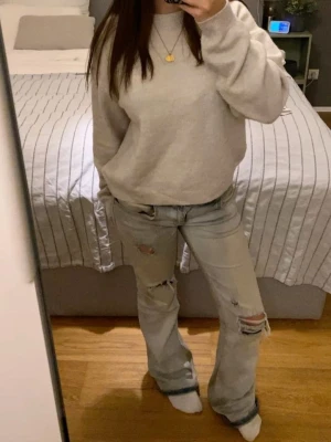 Ljusblå slitna bootcut jeans - Säljer ett par ljusblå bootcut jeans med slitningar och hål på benen. Jeansen har en avslappnad passform och är perfekta för en casual look. Inga synliga loggor eller märken. Materialet känns som klassisk denim.