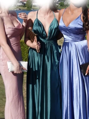 Mörkgrön balklänning - Satin Moa dress från Ivory Field  - Säljer en mörkgrön balklänning från Ivory Field (Satin Moa dress) Klänningen är i nyskick då den endast använts en gång och har blivit kemtvättad efteråt. Ny klänning från hemsidan kostar 2500 kr. Klänningen har en v-ringning, smala axelband, slits på sidan och är tillverkad i ett satin material. 