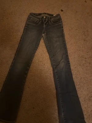 Mörkblå bootcut jeans - Säljer ett par mörkblå bootcut jeans med slitningar och klassisk femficksdesign. Jeansen har låg midja och kontrastsömmar för en snygg look. Perfekta till sneakers eller boots för en avslappnad stil.