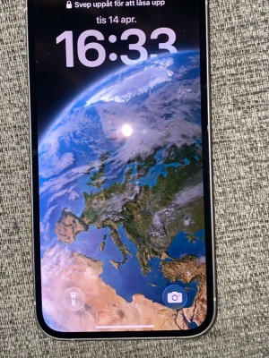 IPhone 13 - Snygg vit iPhone med stilren design och rundade hörn. Baksidan är i glas och har två stora kameralinser samt Apple-loggan i mitten. Telefonen har en stor skärm med tunna kanter och modern look.