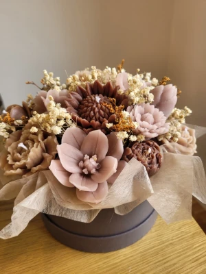 Bukett med blomformade ljus - Unik bukett med handgjorda blomformade ljus i olika nyanser av brunt och beige, arrangerade i en rund mörk ask. Ljusen är detaljerade och ser ut som blommor, blandat med torkade växter för en dekorativ look. Perfekt som inredningsdetalj eller present. Stl m på boxen