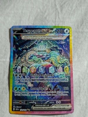 Terapagos ex holo Pokémonkort (SIR) - Holografiskt Pokémonkort med Terapagos ex från Scarlet & Violet-serien. Kortet har en färgstark och skimrande design med hexagonala kristaller och detaljerad illustration. Perfekt för dig som samlar eller spelar Pokémon TCG.