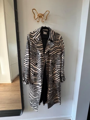 Zebramönstrad kappa By Malene Birger - Snygg zebramönstrad kappa från By Malene Birger med svartvitt mönster och klassisk krage. Kappan har knäppning framtill och är helfodrad. Perfekt statement-plagg för dig som vill sticka ut med din stil.