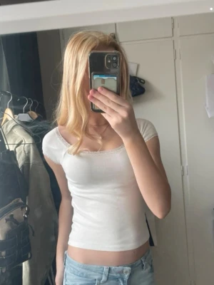 Vit croppad topp med spetskant - Säljer en enkel och fräsch vit croppad topp med korta ärmar och fin spetskant vid halsringningen. Perfekt till jeans eller kjol för en clean look. Superenkel att matcha och passar till alla tillfällen!