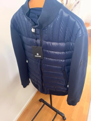  Mackage - Snygg mörkblå pufferjacka från Mackage med quiltad front och släta ärmar. Jackan har ribbad krage, dragkedja framtill och två fickor med dragkedja. Mackage-logga på ärmen ger en exklusiv touch. Perfekt för kalla dagar och riktigt stilren storlek XXL men passar som XL 