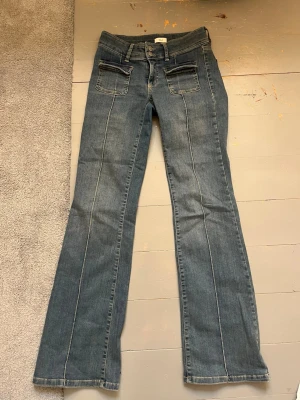 Blå bootcut jeans med fickor - Säljer ett par klassiska blå bootcut jeans med fram- och bakfickor samt markerade sömmar längs benen. Jensen är låg midjade och stretchiga.