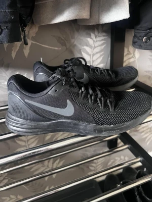 Svarta Nike Lunarlon sneakers - Snygga svarta Nike Lunarlon sneakers med mesh-ovandel och klassisk grå swoosh på sidan. Skorna har låga skaft, svarta skosnören och en bekväm, dämpad sula. Perfekta för dig som gillar sportig och stilren look.
