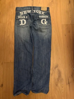Dolce & Gabbana New York jeans - Unika blå jeans från Dolce & Gabbana med stora broderade bokstäver och texten 'NEW YORK' på baksidan. Bakfickorna har tydliga D&G-loggor och detaljerade sömmar. 