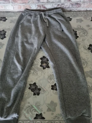 Grå mjukisbyxor från Polo Ralph Lauren - Snygga grå mjukisbyxor från Polo Ralph Lauren med dragsko i midjan och resår vid bensluten. Byxorna har sidofickor och den klassiska lilla loggan broderad på vänster sida. Perfekta för chill dagar eller när du vill vara bekväm.