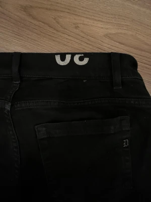 Svarta jeans från dondup - Säljer ett par svarta jeans från dondup med klassisk femficksmodell och raka ben. Jeansen har bälteshällor och knappgylf. Materialet är denim i bomull med en snygg tvättad look. Perfekta för en avslappnad och trendig stil.