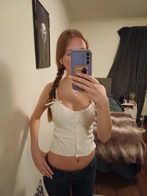 Vit ribbad linnetopp med rosetter - Söt vit ribbad linnetopp med knappar framtill och små rosetter på axelbanden. Toppen har en croppad passform och smala axelband. Perfekt nu till sommaren 