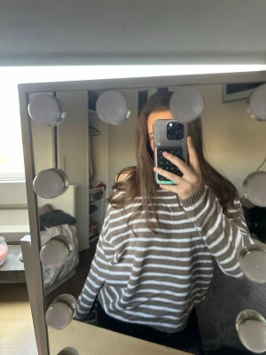 Randig beige och vit stickad tröja - Säljer en oversized stickad tröja med breda beige och vita ränder. Tröjan har rund halsringning och långa ärmar, perfekt för en avslappnad och trendig look. Materialet känns mjukt och bekvämt mot huden.