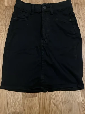 Svart jeanskjol med fickor - Säljer en svart jeanskjol från Perfect Jeans. Kjolen har klassisk femficksdesign, knapp och dragkedja framtill samt bakfickor. Rak passform och midjehög modell som passar till det mesta. Perfekt basplagg i garderoben.