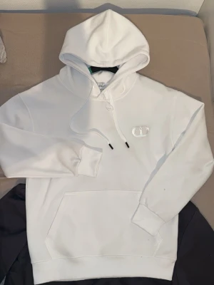 D*or Vit hoodie - Säljer en clean vit hoodie från D*or med broderad. Hoodien har klassisk känguruficka, dragsko i huvan och ribbade muddar. Perfekt för dig som gillar stilrena plagg med exklusiv känsla.