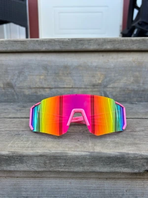 Rosa skiftande Sportglasögon Färgglada sportiga solglasögon - Säljer ett par riktigt färgstarka och sportiga solglasögon med glas som skiftar i röd, orange, gul, grön, blå och rosa båge. Glasögonen har en futuristisk, bred skärmform som ger maxad täckning och cool look. Perfekta för dig som vill sticka ut i sommar!