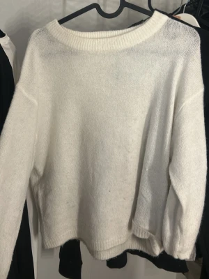 Vit stickad - Mysig vit stickad tröja med bred ribbad rundhals och avslappnad passform. Tröjan har långa ärmar och är tillverkad i ett mjukt material som känns skönt mot huden. Perfekt för lager på lager och en clean look.