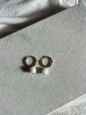 Guldiga hoops med vita pärlor - Snygga örhängen i guldton med rund form och hängande vita pärlor. Perfekta för att ge en elegant touch till din look. Klassisk design som passar till många stilar.