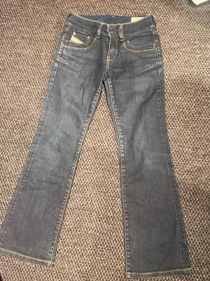 Mörkblå bootcut jeans från Diesel - Säljer ett par mörkblå bootcut jeans från Diesel med klassiska fem fickor och kontrastsömmar. Jeansen har en snygg tvätt och är tillverkade i slitstark denim. Perfekta för dig som gillar en tidlös och avslappnad stil.