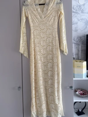 Lång ljus spetsklänning med v-ringning - Elegant långklänning i ljusgul ton med v-ringad hals och långa ärmar. Klänningen är helt täckt av  spets med blommigt mönster och den har en väldigt fin passform och formar sig efter kroppen. Perfekt för speciella tillfällen när du vill känna dig extra fin såsom bal/student. Köpte den för 1300 ungerfär andvänt den 1 gång