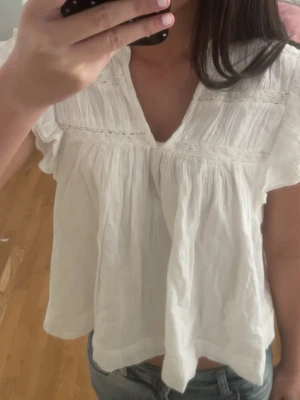 Vit blus - Söt vit blus från Gina tricot med v-ringning och volangdetaljer vid axlarna. Blusen har korta ärmar och är tillverkad i ett lätt, luftigt tyg som känns perfekt för sommaren. 