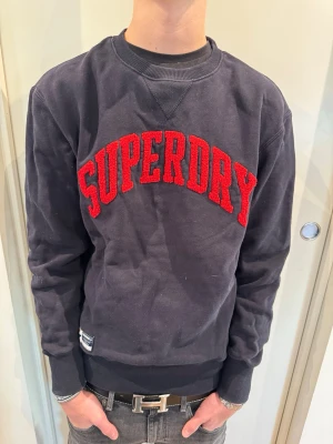 Blå Superdry Sweatshirt - Säljer en snygg blå Superdry sweatshirt i storlek S. Modellen på bilden är 180 cm lång och väger 65 kg.