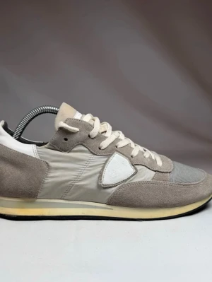 Philippe Model - Stilrena sneakers från Philippe Model i grått och beige med ovandel i mocka, nylon och mesh. Klassisk låg modell med vita snören och ikonisk sköld på sidan. Perfekta för en clean och avslappnad look.