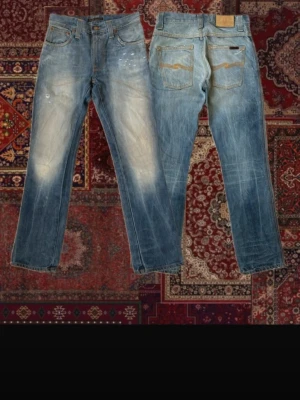 Nudie Jeans - Säljer ett par Nudie Jeans, en aning bootcut. Jeansen har tydliga slitningar och snygg tvätt. Jeansen är i denim och har en vintagekänsla. OBS finns vita fläckar på låren/knä men de syns knappt.                        A: 37,5cm  B: 102cm.         