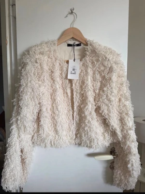 Krämvit fluffig kofta - Säljer en supermjuk och fluffig krämvit kofta med lång ärm och öppen framtill. Koftan har axelvaddar och en lurvig textur som ger en trendig look och är perfekt för dig som vill sticka ut. Passar till både jeans och kjol för en avslappnad men stylish vibe. Helt ny med prislapp. 🩷599 nypris 