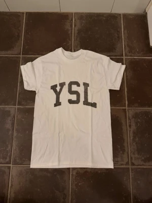 YSL t shirt - Riktigt fet och eftertraktad t shirt med YSL loggan i storlek S! Helt nytt skick! Lite osäker på äktheten eftersom lappen i nacken saknas så därför är priset just nu på 499kr nypris runt 3000kr! Tveka inte med att ställa frågor! 