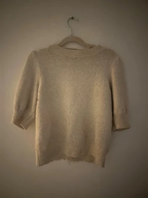 Beige stickad tröja med puffärm - Mysig beige stickad trekvart tröja med korta puffärmar och ribbstickade muddar vid ärmslut och nederkant. Tröjan har lite noppring men inga hål eller fläckar💕