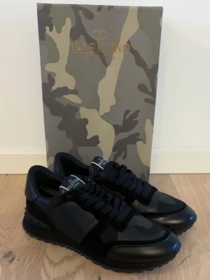  Valentino Garavani rockrunners  - Säljer ett par riktigt schysta svarta sneakers från Valentino Garavani med en mix av mocka och läderdetaljer. Skorna har kamouflagemönster på ovandelen, svarta skosnören och en chunky sula med nitar på hälen. Perfekta för dig som gillar exklusiv streetstyle. Dom är sparsamt använda och är i topp skick. Sko lådan och crease skydd tillkommer. Priset kan diskuteras. Vid någon som helst fråga hör av er ☺️