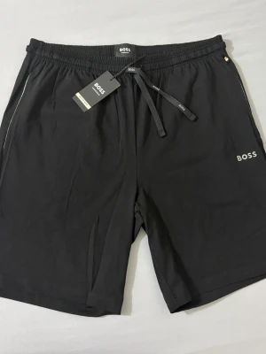 Svarta shorts från BOSS  - Svarta shorts från BOSS. Klassisk design med diskret BOSS-logga på vänster ben. Tillverkade i mjukt bomullsmaterial för en skön och avslappnad känsla. Perfekta för sommardagar eller chill hemma.