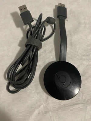 Google Chromecast, generation 2.  - Google Chromecast NC2-6A5, generation 2. Ansluts till TV:ns HDMI-port. Strömförsörjning via USB eller valfri strömadapter som man har liggandes hemma.   Google Chromecast är en mediaspelare som ansluts till din TV:s HDMI-port. Den låter dig streama underhållning direkt från din telefon, surfplatta eller dator till din TV. Chromecast är kompatibel med en mängd olika appar och tjänster, vilket gör det enkelt att titta på filmer, serier, lyssna på musik och mycket mer på din TV.  Fullt fungerande o