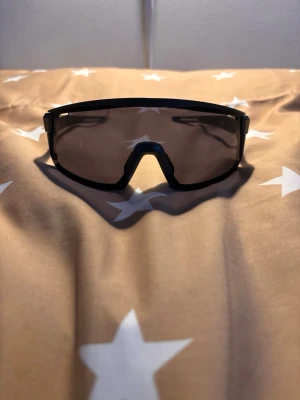 Svarta sportiga solglasögon från EQPE - Säljer ett par svarta sportiga solglasögon från EQPE med breda, rektangulära linser och mattsvart båge. Glasögonen har en modern, kantig design och passar perfekt för utomhusaktiviteter. Snygg och funktionell accessoar för dig som gillar sportig stil.