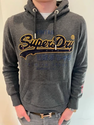 Mörkgrå Superdry hoodie med tryck - Mörkgrå hoodie från Superdry i storlek S modellen är 173cm och väger 62 kg så 