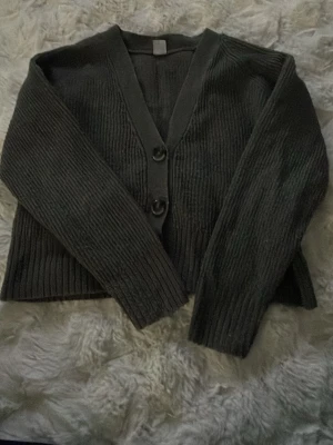 Mörkgrå ribbad kofta från Lindex - Snygg mörkgrå ribbad kofta från Lindex med tre stora knappar framtill. Koftan har v-ringning, långa ärmar och är tillverkad i ett mjukt stickat material. Perfekt att slänga över en t-shirt för en chill look. Pris 20kr