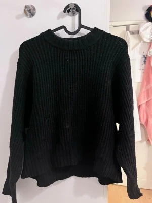 Svart stickad tröja - Mysig svart stickad tröja med fin passform och bred ribbstickning. Tröjan har rund halsringning och långa ärmar, perfekt för lager på lager och en avslappnad look. Passar till allt och är superenkel att styla. Finns en liten fläck på framsidan, nästan helt 100 på att det går bort i tvätt