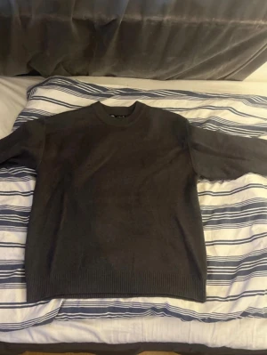 Mörkgrå stickad tröja - En enkel och stilren mörkgrå stickad tröja med rund halsringning och ribbade muddar vid ärmslut och nederkant. Perfekt basplagg för lager på lager och passar till det mesta. Tröjan har en rak passform och är mjuk i materialet.