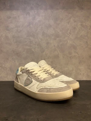 Philippe Model - Snygga sneakers från Philippe Model i vitt och ljusgrått med detaljer i mocka och canvas. Skorna har en låg siluett, vita snören och en ljusblå detalj på hälen. Perfekta för en clean och stilren look. I bra skick! Nypris 3000:- (har ej kvar boxen)