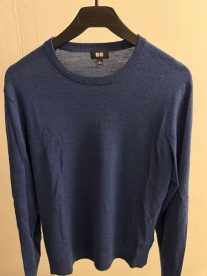 Blå tunn merino ull tröja från Uniqlo - Snygg blå långärmad tröja från Uniqlo i tunn och mjuk kvalitet (merinoull). Tröjan har rund halsringning och en enkel, stilren design som passar perfekt till jeans eller chinos. Materialet känns lätt och skönt mot huden.