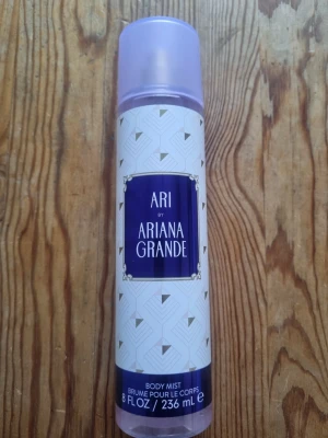 Ari by Ariana Grande Body Mist - Fräsch body mist från Ariana Grande i doften Ari. Flaskan är cylinderformad med lila lock och vit etikett med geometriskt mönster och lila detaljer. Innehåller 236 ml och har en modern, stilren design som känns lyxig och trendig.