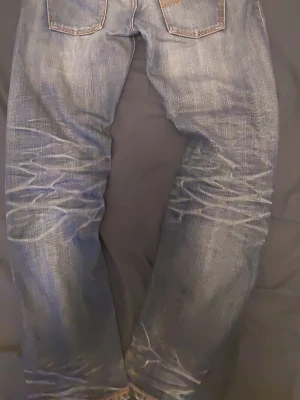 Nudies washed - Säljer ett par blå jeans med snyggt sliten tvätt och raka ben. Jeansen har klassiska bakfickor och kontrastsömmar. Materialet är denim i bomull och de har en cool vintagekänsla med tydliga slitningar och whiskers-effekt. Tyvärr hål i högra ficka men går säkert att sy igen