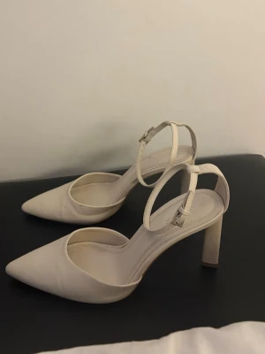 Beige pumps med ankelrem - Så snygga och stilrena klackskor från Stradivarius i vit kräm färg.  Klassisk spetsig tå (pointed toe) och ankelrem som ger en elegant och feminin look.  Perfekta till långa jeans!!! fest, student, bröllop eller sommarens tillställningar 🤍  Använda endast inomhus men i fint skick – mindre tecken på användning finns (se bilder), inget som påverkar helhetsintrycket.  Bekväma att gå i och lätta att matcha med både klänning och byxor.  klackskor högklackat pumps spetsig tå / pointed toe ankelrem / a