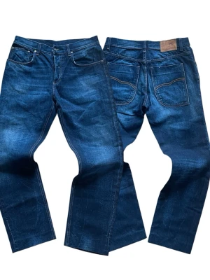 Blå raka jeans från moods of norway - Säljer ett par klassiska blå jeans från moods of norway med raka ben och snygga slitningar. Jeansen har fem fickor, kontrastsömmar och en patch i läderimitation bak i midjan. Tillverkade i slitstark denim som ger en cool vintagekänsla.