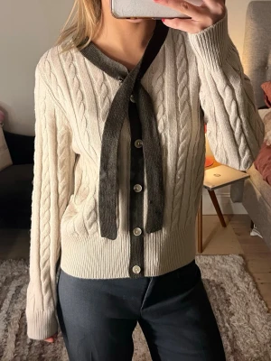 Beige kabelstickad kofta med knytband - Kabelstickad beige kofta med mörkbruna detaljer och knytband vid halsen. 100% ull och köpt på arkivet som ny för 899kr. 💛💛💛💛